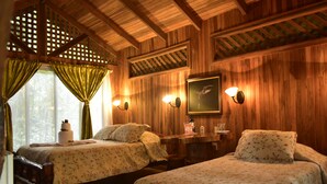 A wooden cabin room with two beds, a wooden desk, and a window with green curtains. - Arenal Oasis (La Fortuna)