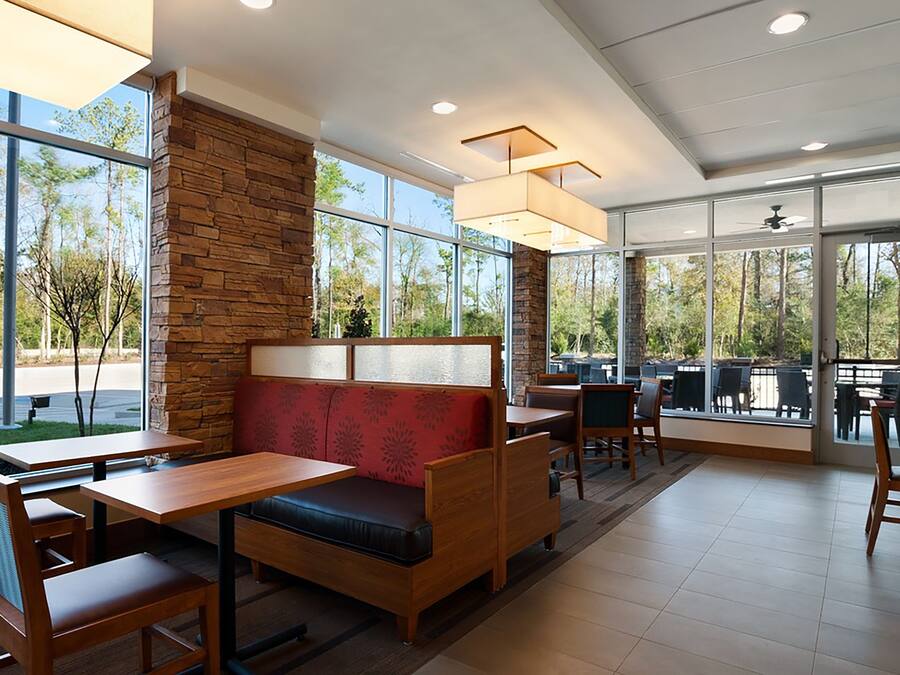 Un restaurant avec des tables et des bancs en bois, des murs en pierre, de grandes fenêtres et une vue sur les arbres.