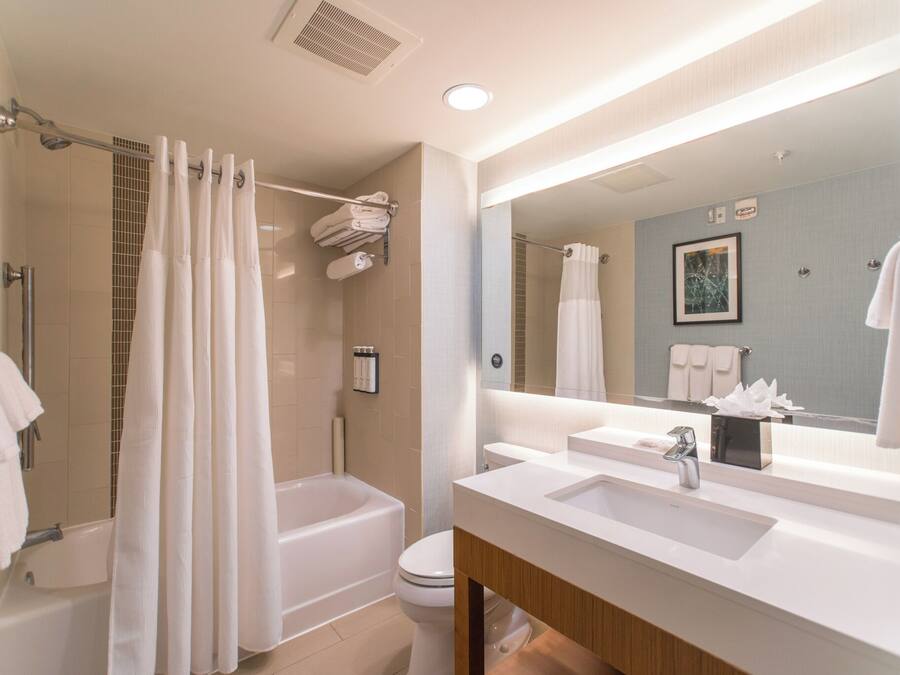 A modern bathroom with a bathtub, shower, toilet, and a large mirror above the sink.