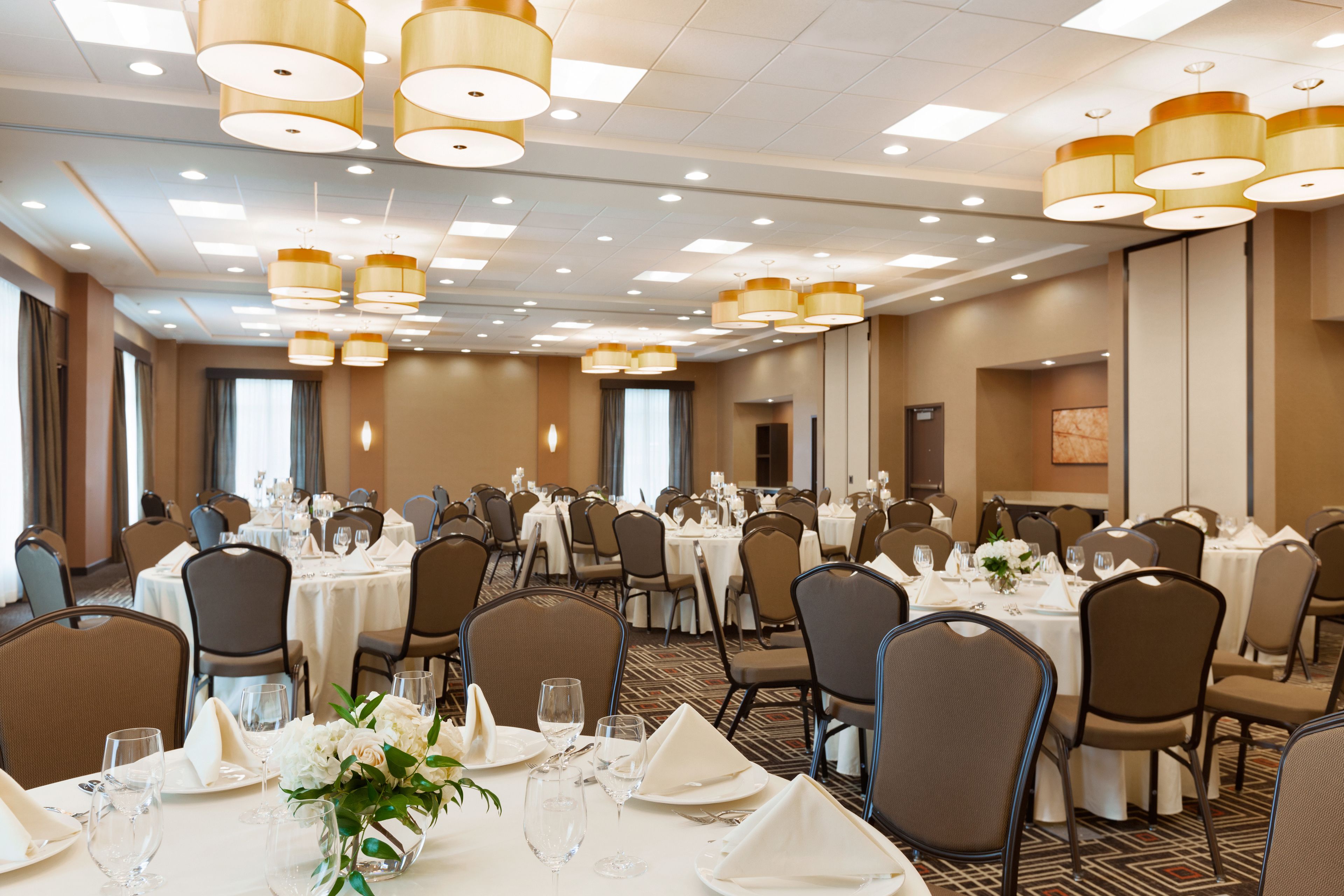 Un salón de banquetes con varias mesas redondas dispuestas para comer, equipado con sillas, mesas y centros de mesa.