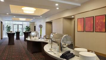 A hotel reception area with a buffet setup, including a food display, plates, and a water dispenser.