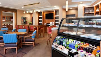 A hotel restaurant with wooden furniture, a glass display case with food and drinks, and a wall-mounted TV.