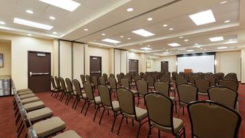 Un salón de conferencias con filas de sillas y una pantalla para proyector.