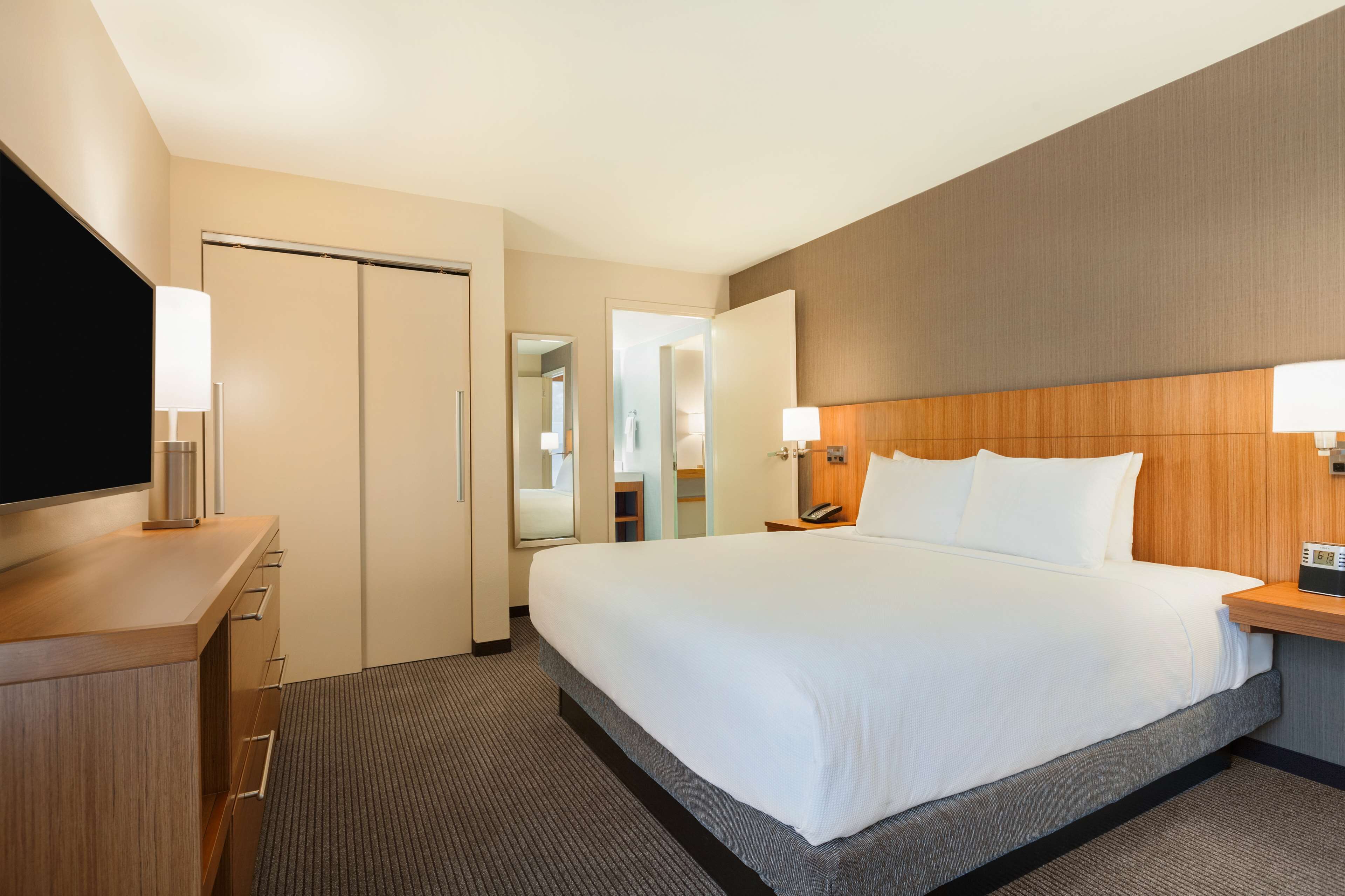 Quarto de hotel com uma cama grande, uma escrivaninha de madeira, uma televisão de tela plana e um espelho.