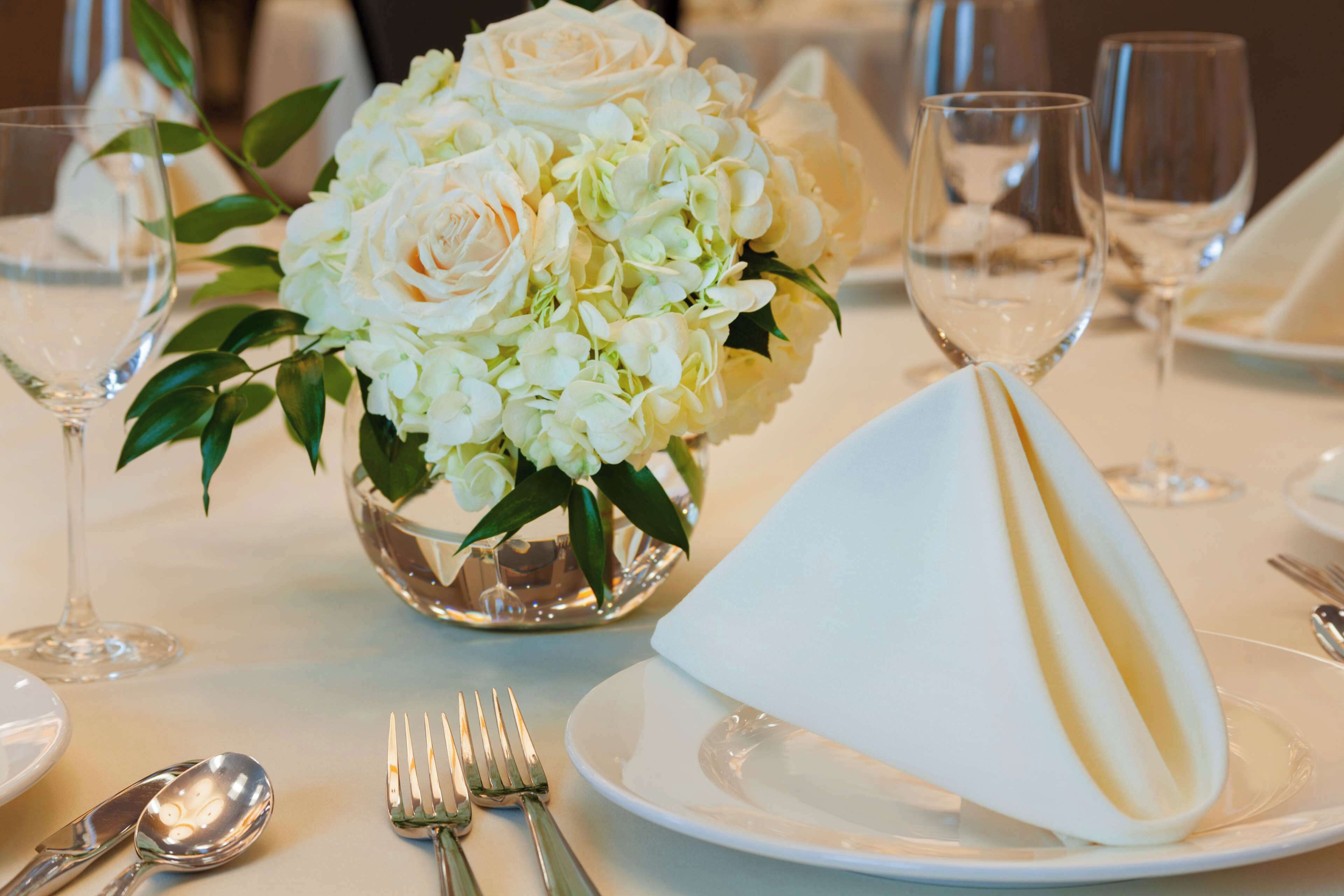 Una mesa dispuesta para una comida formal, con un centro de mesa de flores blancas, cubiertos y copas de vino.