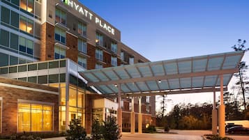 A modern hotel with a covered entrance, large windows, and a well-lit facade.