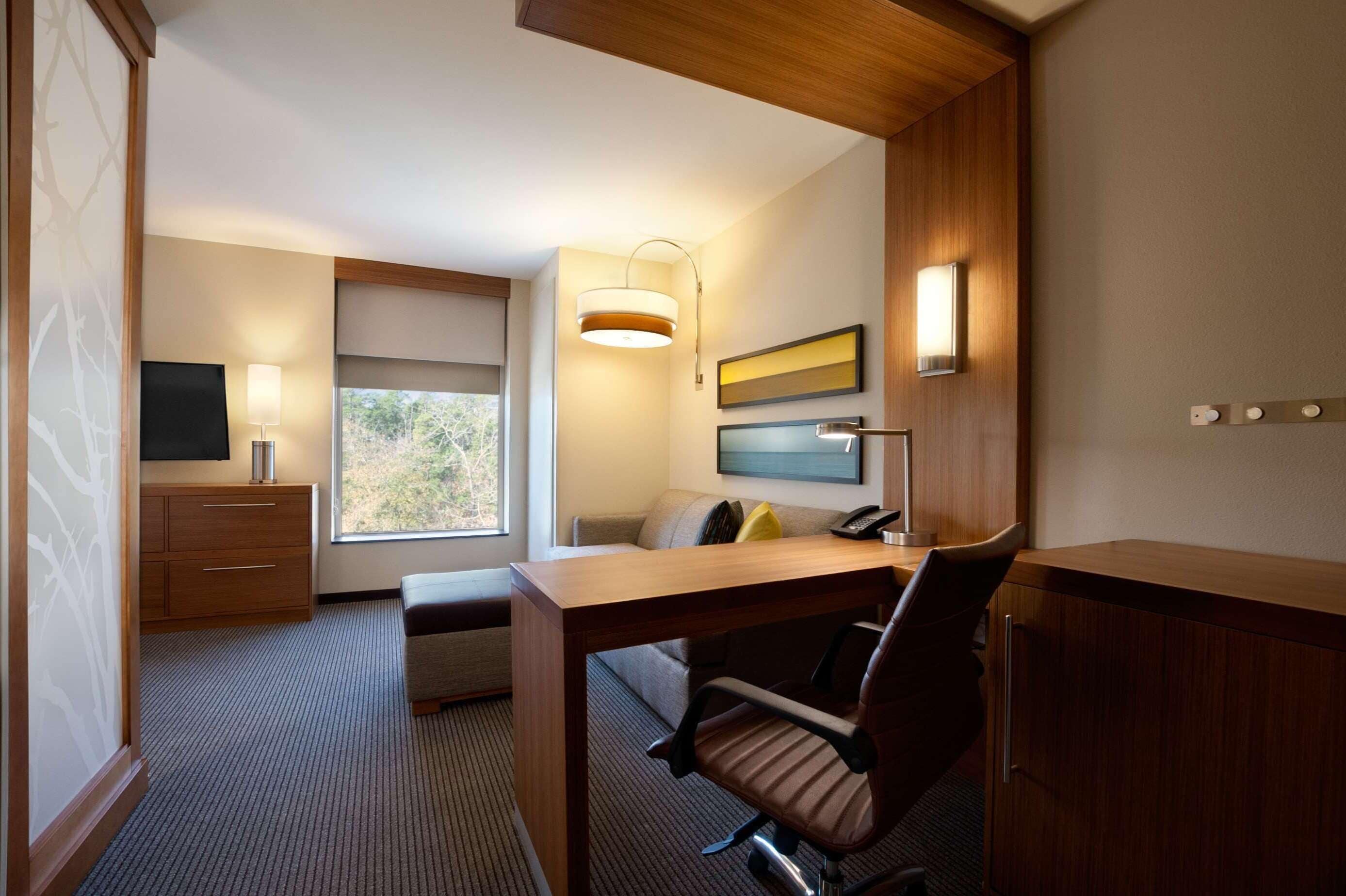 Un espacio de oficina moderno con un escritorio de madera, un sofá cómodo, un televisor y una ventana con vistas.