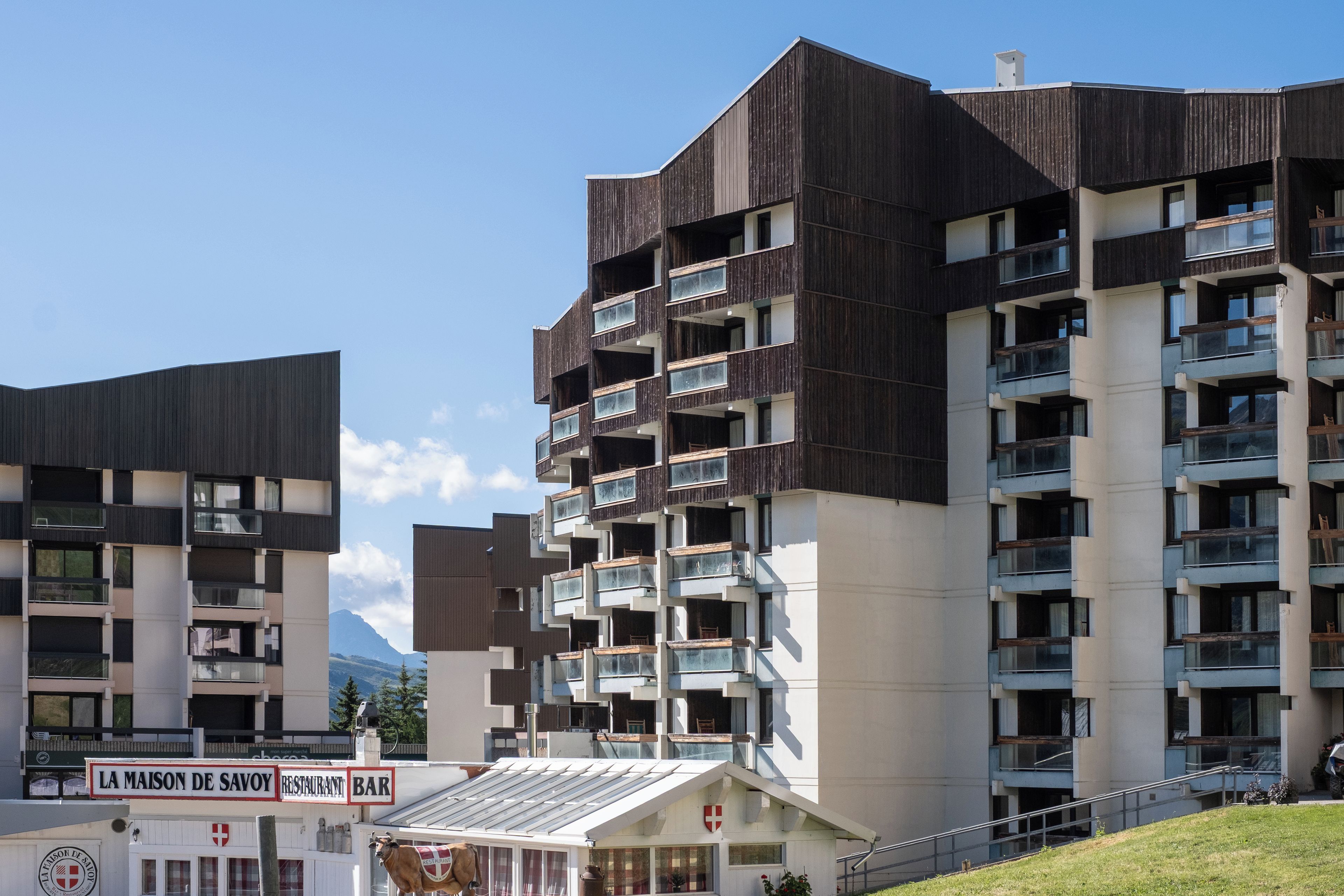 A multi-story building with balconies, a restaurant sign, and a mountain in the background.