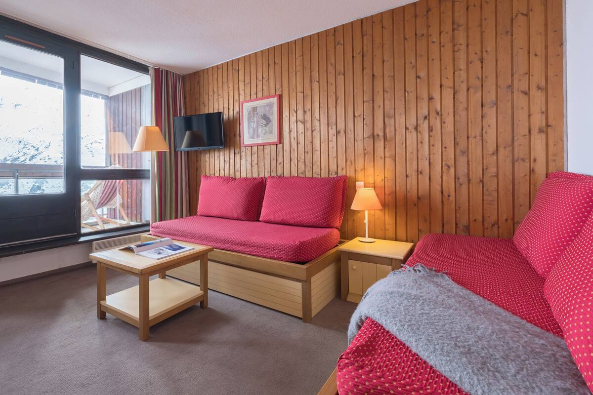 Ett mysigt rum med en väggpanel av trä, en röd soffa, ett litet träbord med en bok och en lampa.