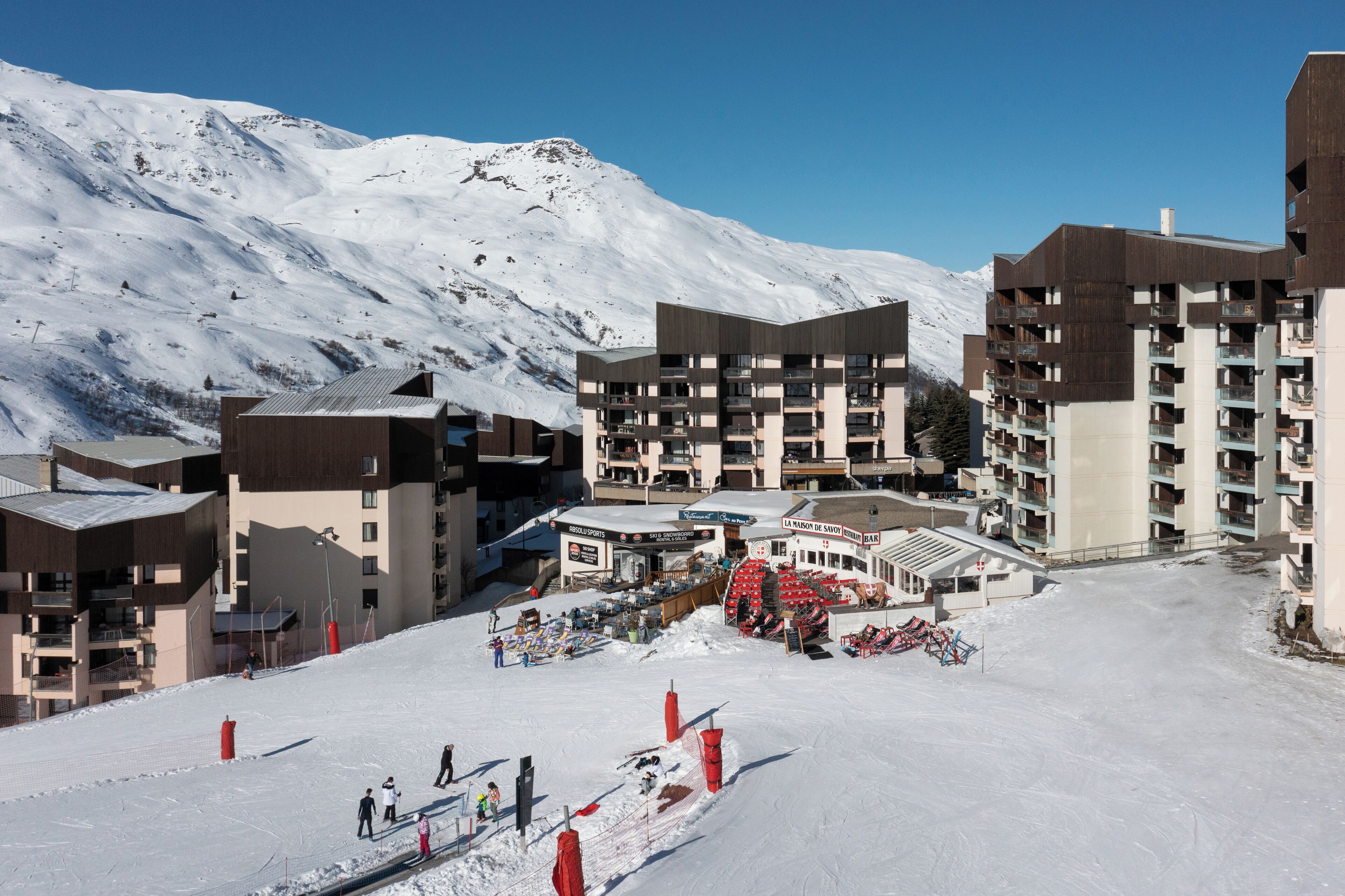 A ski resort with multi-story buildings, a ski lift, and a snow-covered mountain in the background.