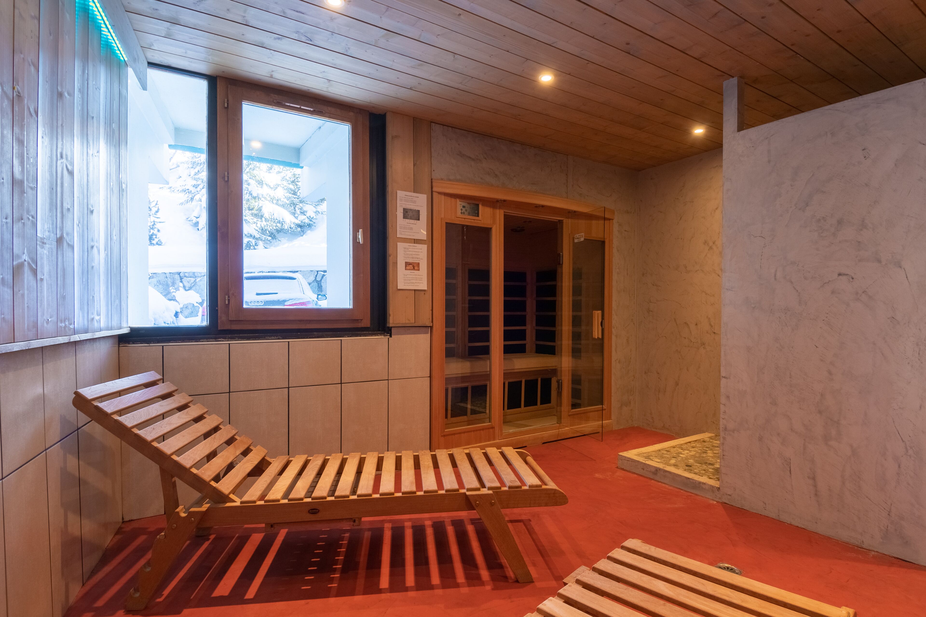 Techo de madera, una ventana con vista a un automóvil, un banco de madera y una puerta con paneles de vidrio.