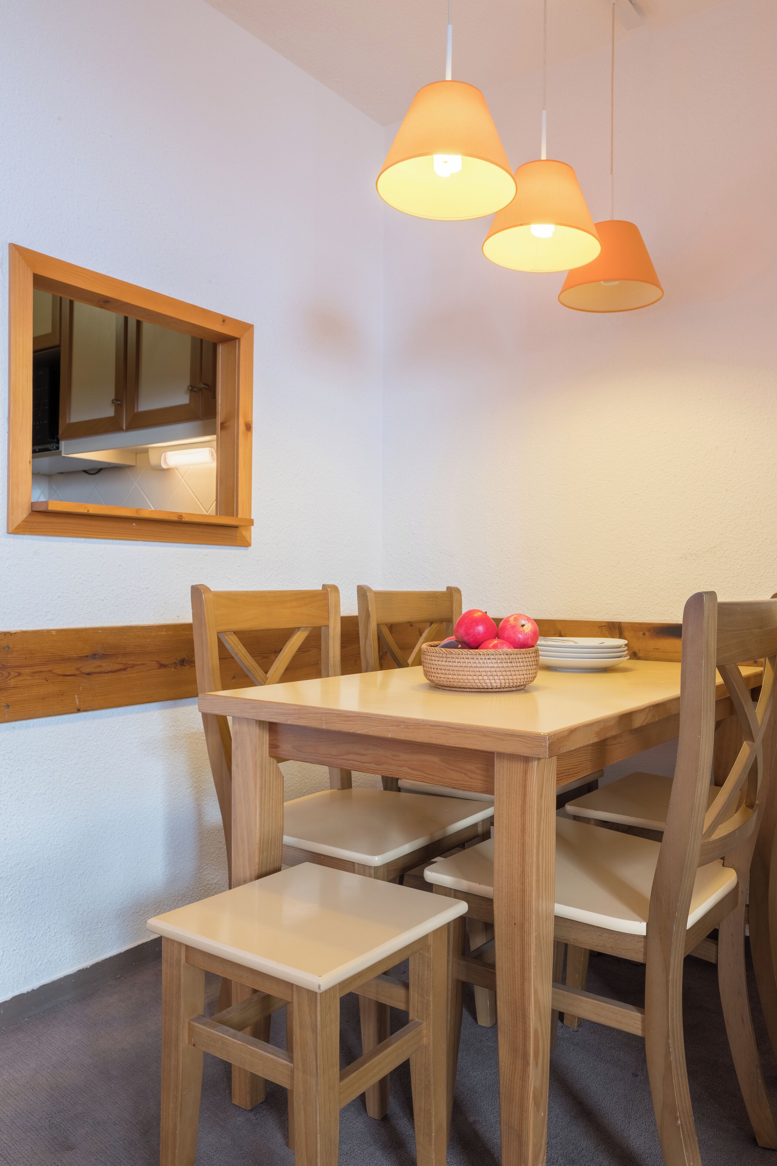 A dining area with a wooden table and chairs, a fruit basket, and pendant lighting.
