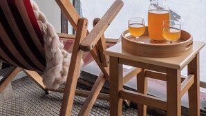 A wooden chair with a striped cushion, a wooden table with a tray holding two glasses and a pitcher of tea, and a snowy mountain view through a window. - Résidence Pierre & Vacances Les Menuires Les Combes (Les Belleville)