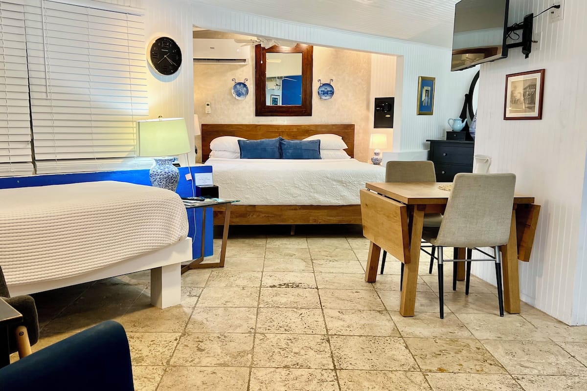 A hotel room with two beds, a desk, a chair, a small table, a clock, and a mirror.