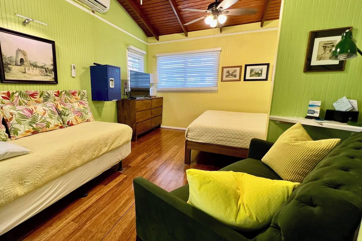 A small, cozy room with two beds, a green sofa, and a wooden dresser.