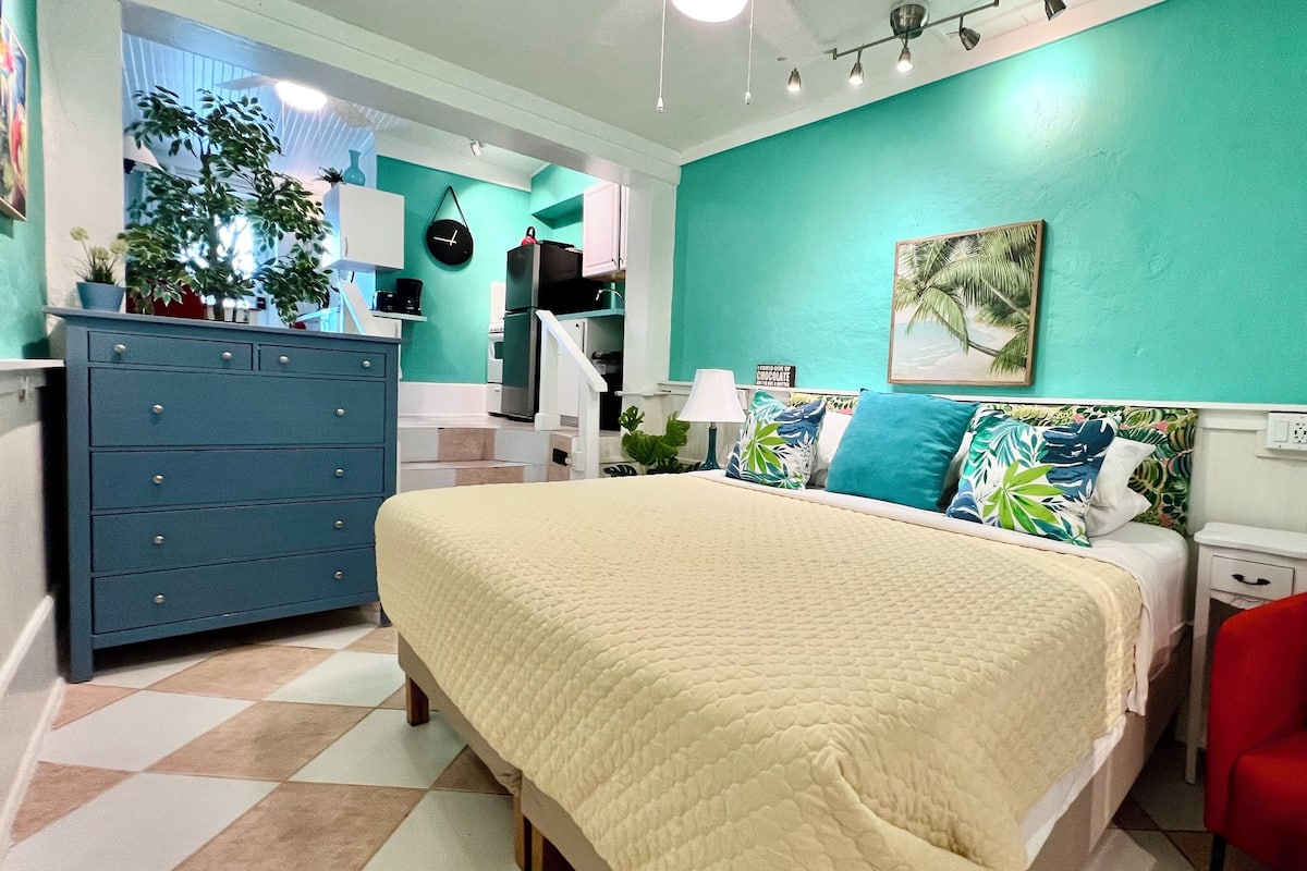 A bedroom with a bed, a dresser, a nightstand, a red chair, a clock, and a painting on the wall.