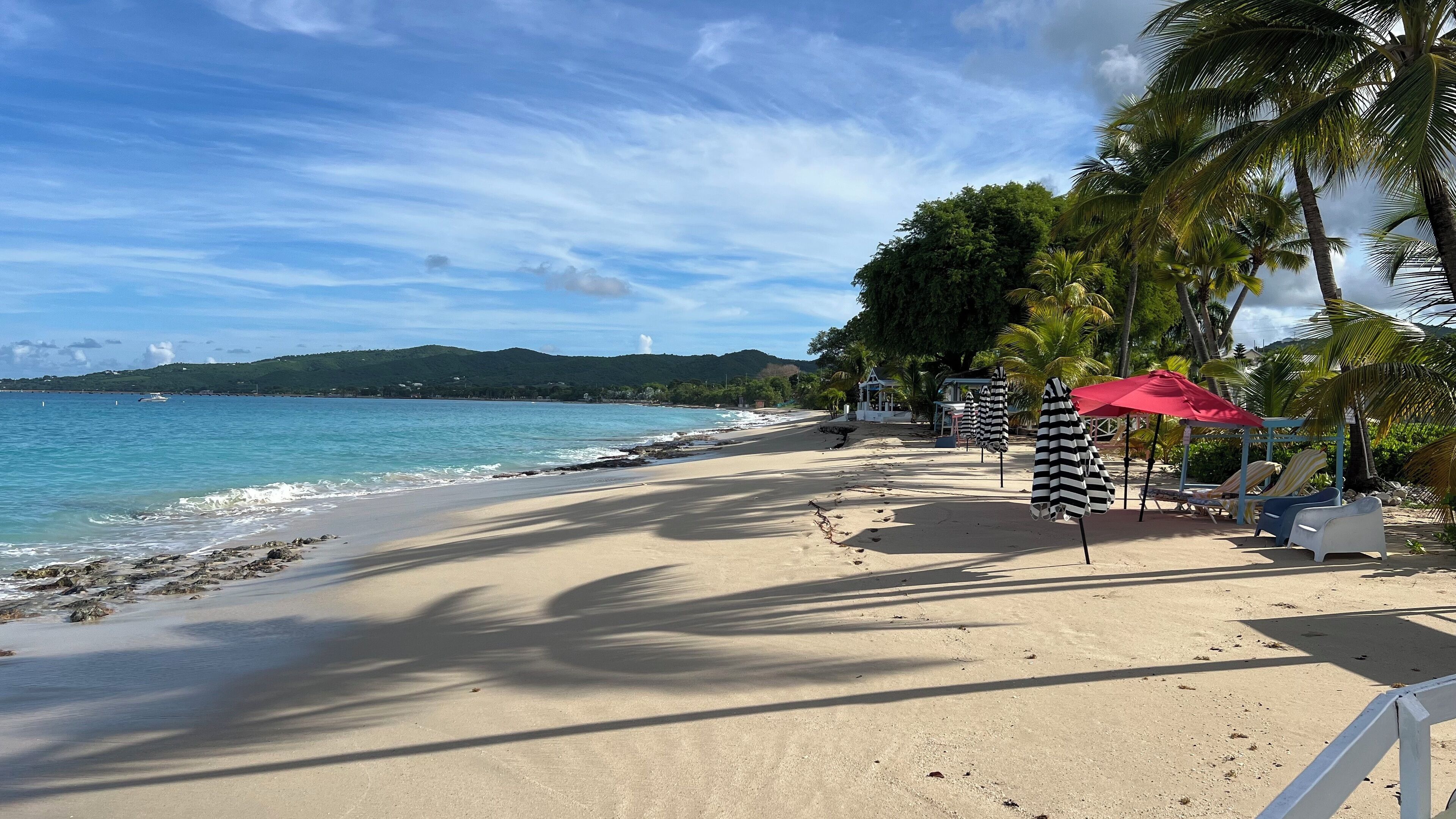 Uma praia com guarda-sóis, cadeiras de espreguiçadeira e vista para o oceano.