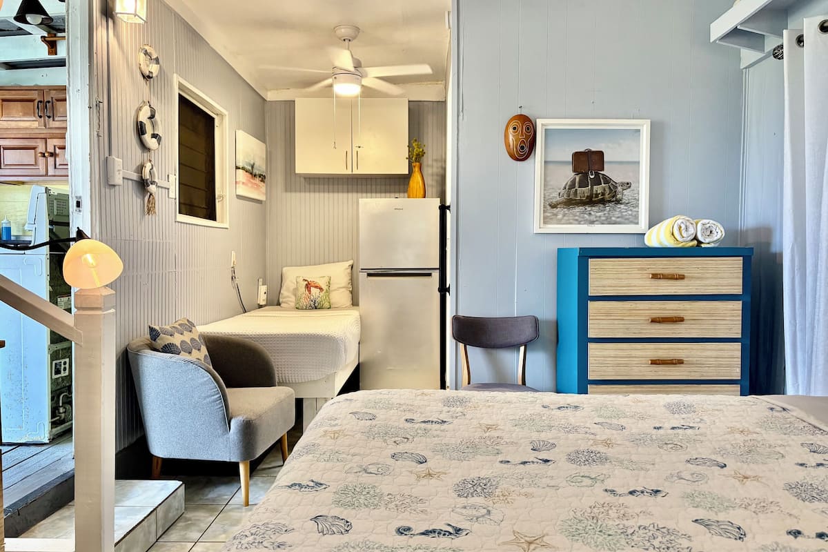 A compact bedroom with a bed, a chair, a dresser, and a ceiling fan.