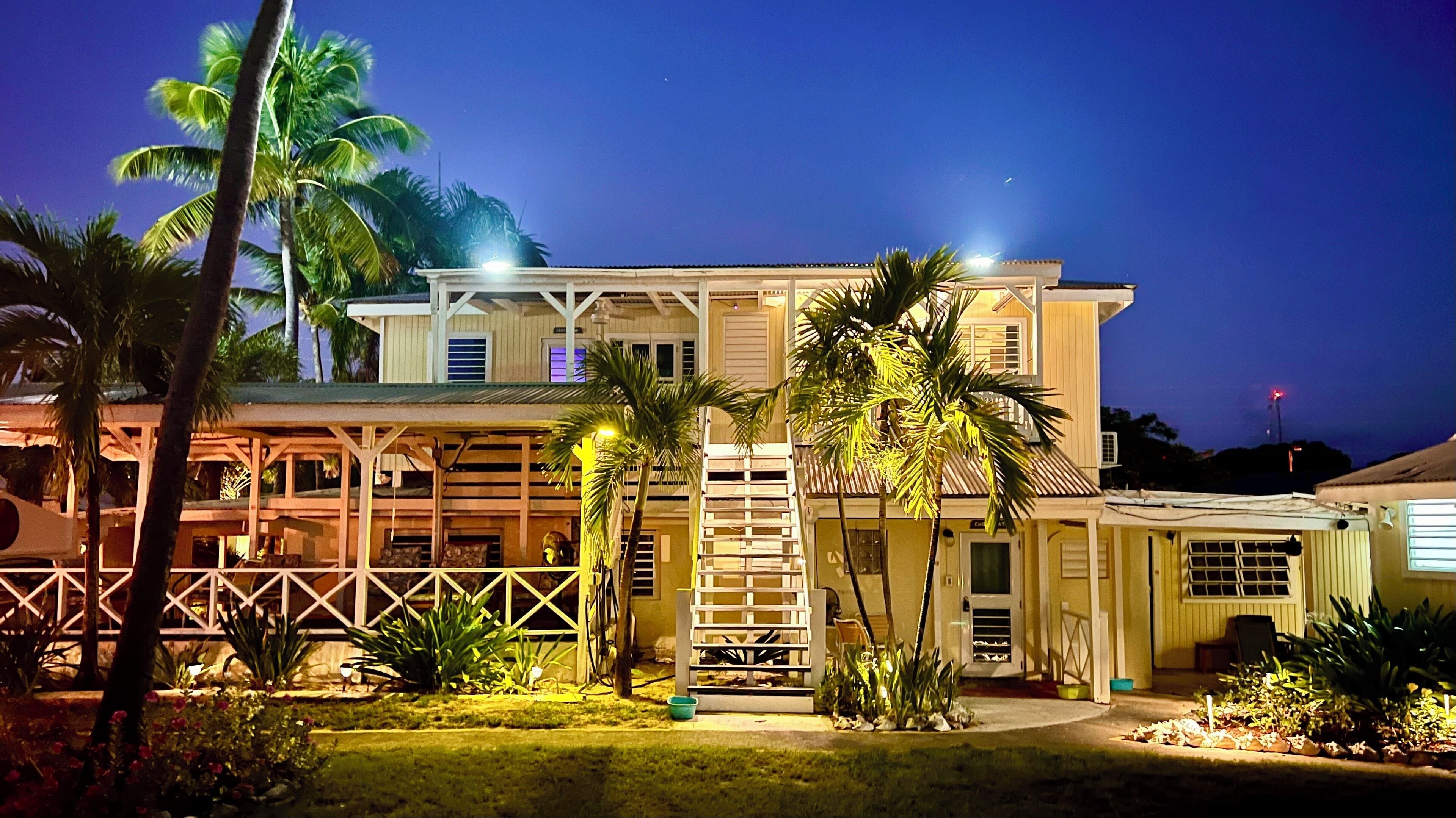 A two-story building with a covered porch and a small garden area with palm trees.