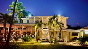 A two-story building with a covered porch and a small garden area with palm trees.