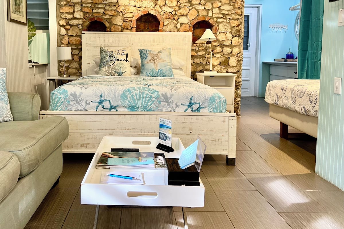 A bedroom with a stone wall, a bed with a blue and white floral bedspread, a nightstand, and a bedside table with a lamp.