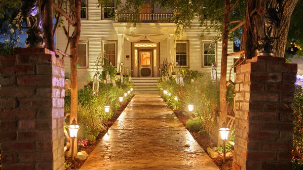 A well-lit pathway leading to a building with a front porch, surrounded by plants and decorative lights. - Bybee's Historic Inn (Central Point)