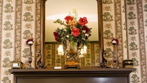 A fireplace with a mirror above it, flanked by patterned wallpaper and decorative items. - Bybee's Historic Inn (Central Point)