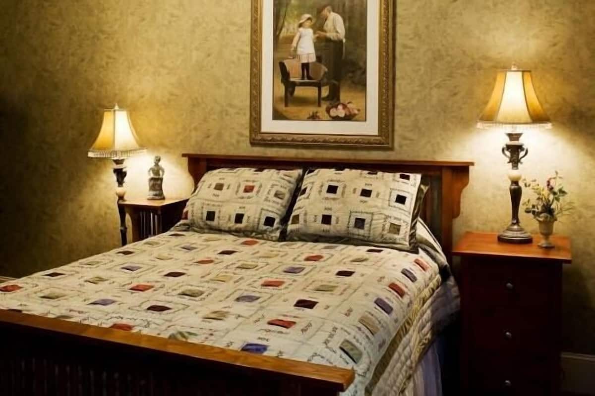 Quarto com uma cama, duas luminárias de cabeceira, um quadro na parede e uma mesa de cabeceira com um vaso.