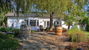 A rustic house with a stone pathway leading to the entrance, surrounded by greenery and two large wooden barrels. - Bybee's Historic Inn (Central Point)