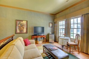 A living room with a sofa, a coffee table, a television, a small table with a vase, and a chair.