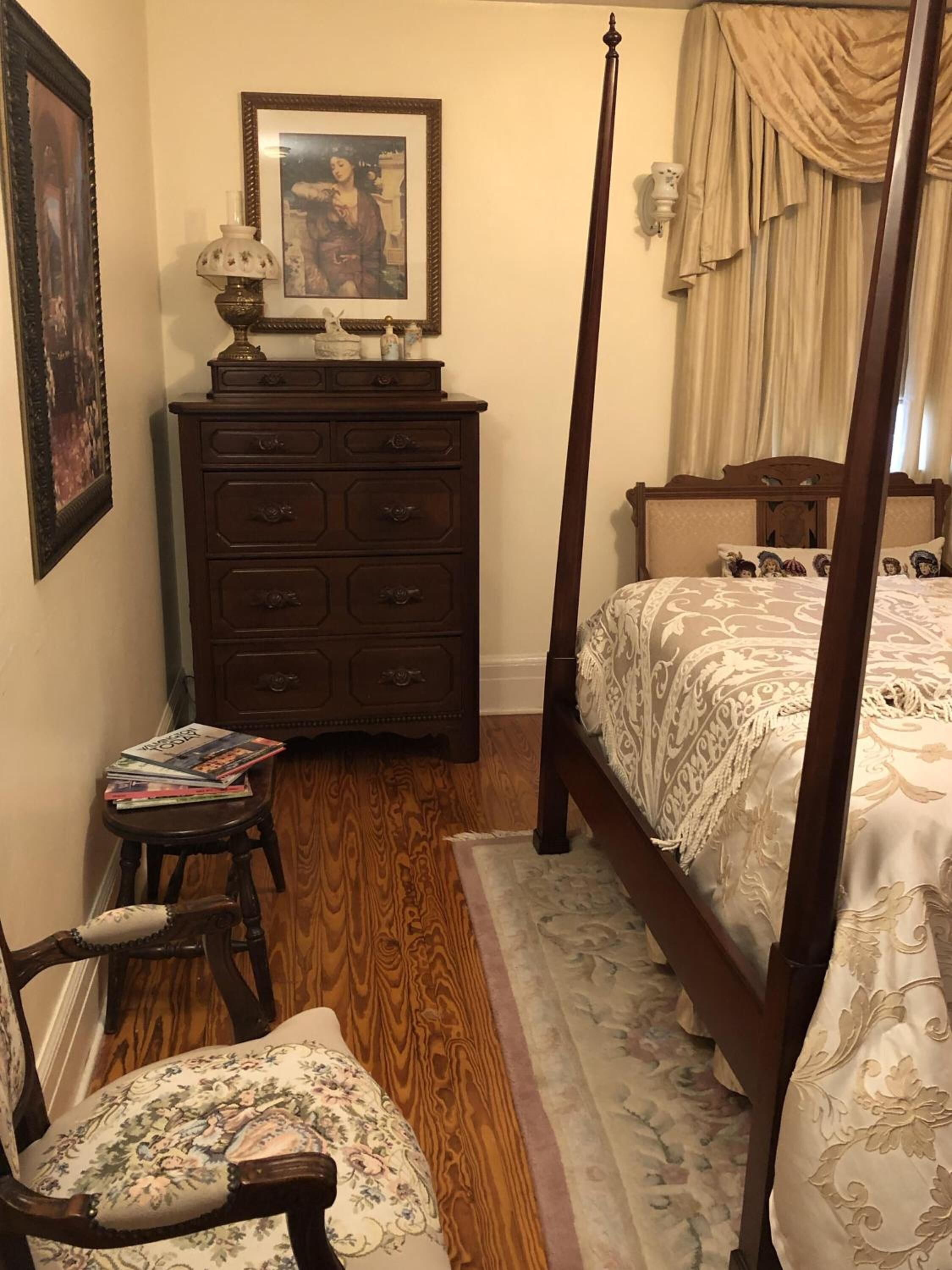 Une chambre à coucher avec un lit à baldaquin, une commode en bois, une chaise et un tableau encadré accroché au mur.