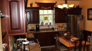 Eine Küche mit dunklen Holzausführungen, einer Granit Arbeitsplatte, einem Edelstahlkühlschrank und einem Essbereich mit Holztisch und Stühlen.