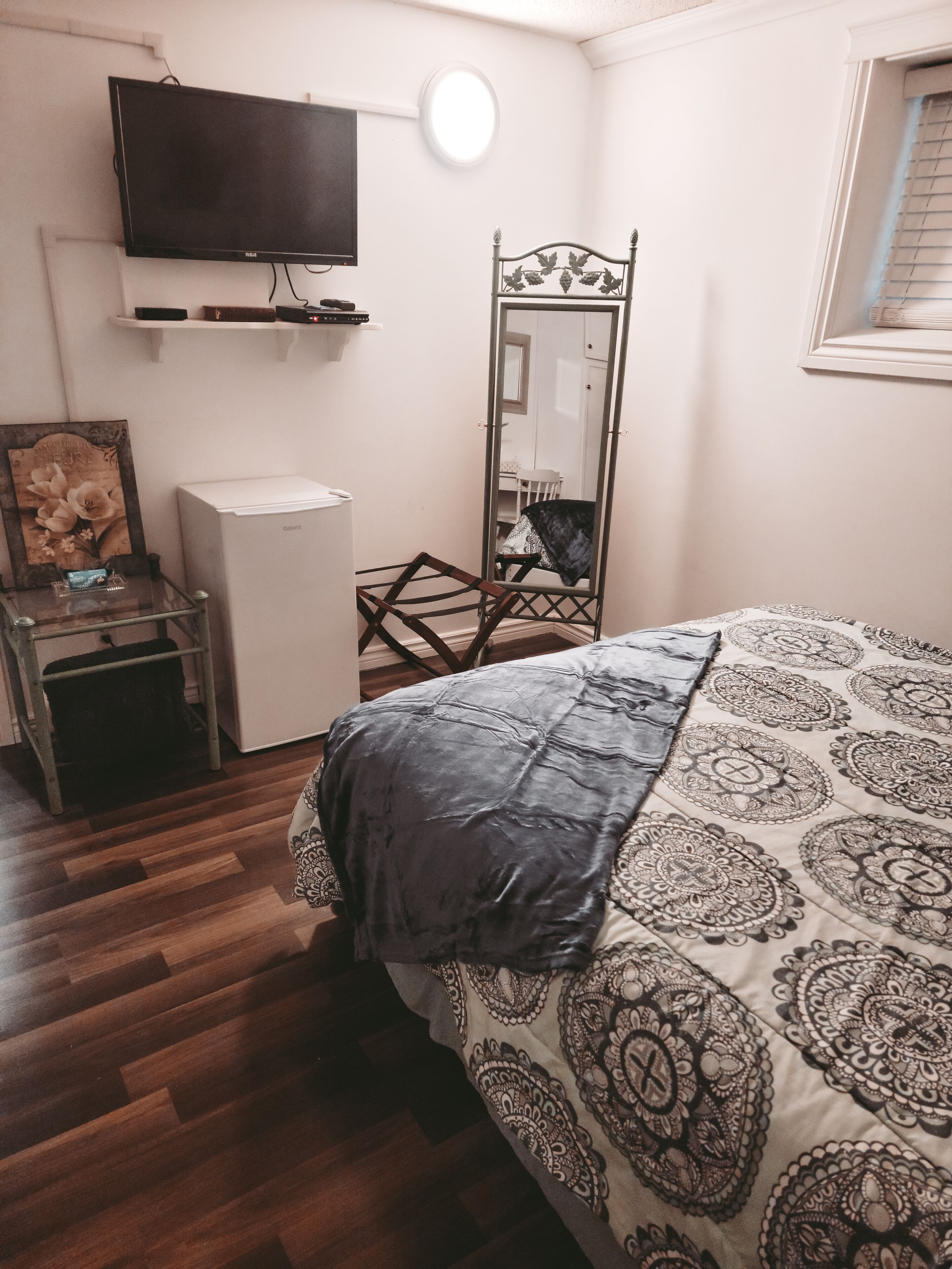 A bedroom with a bed, a television, a mirror, and a small white appliance.