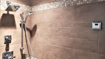 Ducha con cabezal de mano, panel de control en la pared y diseño de azulejos en esquina.