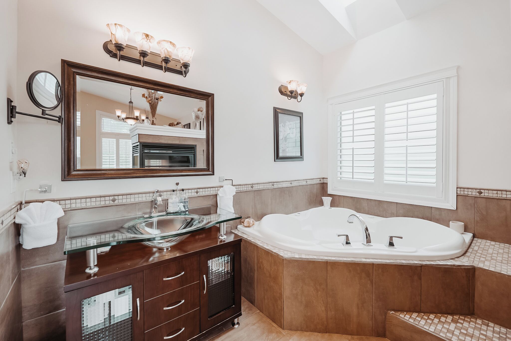 A spacious bathroom with a large bathtub, a glass-enclosed vanity, and a large mirror.