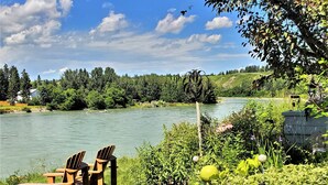 A riverside view with a grassy area, two wooden chairs, and a metal sculpture. - Along River Ridge (Calgary)
