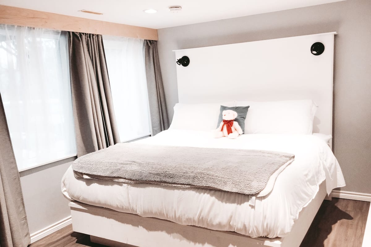 A modern bedroom with a large bed, a headboard, a bedside table, and a window with curtains.