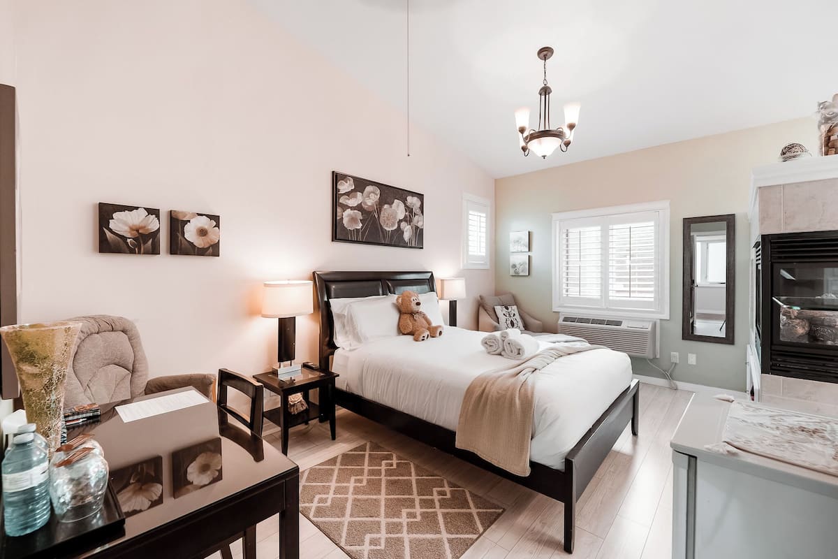 A bedroom with a bed, bedside tables, a desk, a chair, a lamp, a teddy bear, and artwork on the walls.