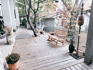 A wooden deck with a rocking chair, potted plants, and a metal fence.