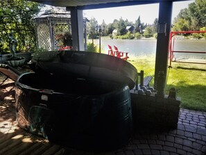 A covered outdoor area with a large black barrel, a gazebo, and a view of a lake with houses in the background.