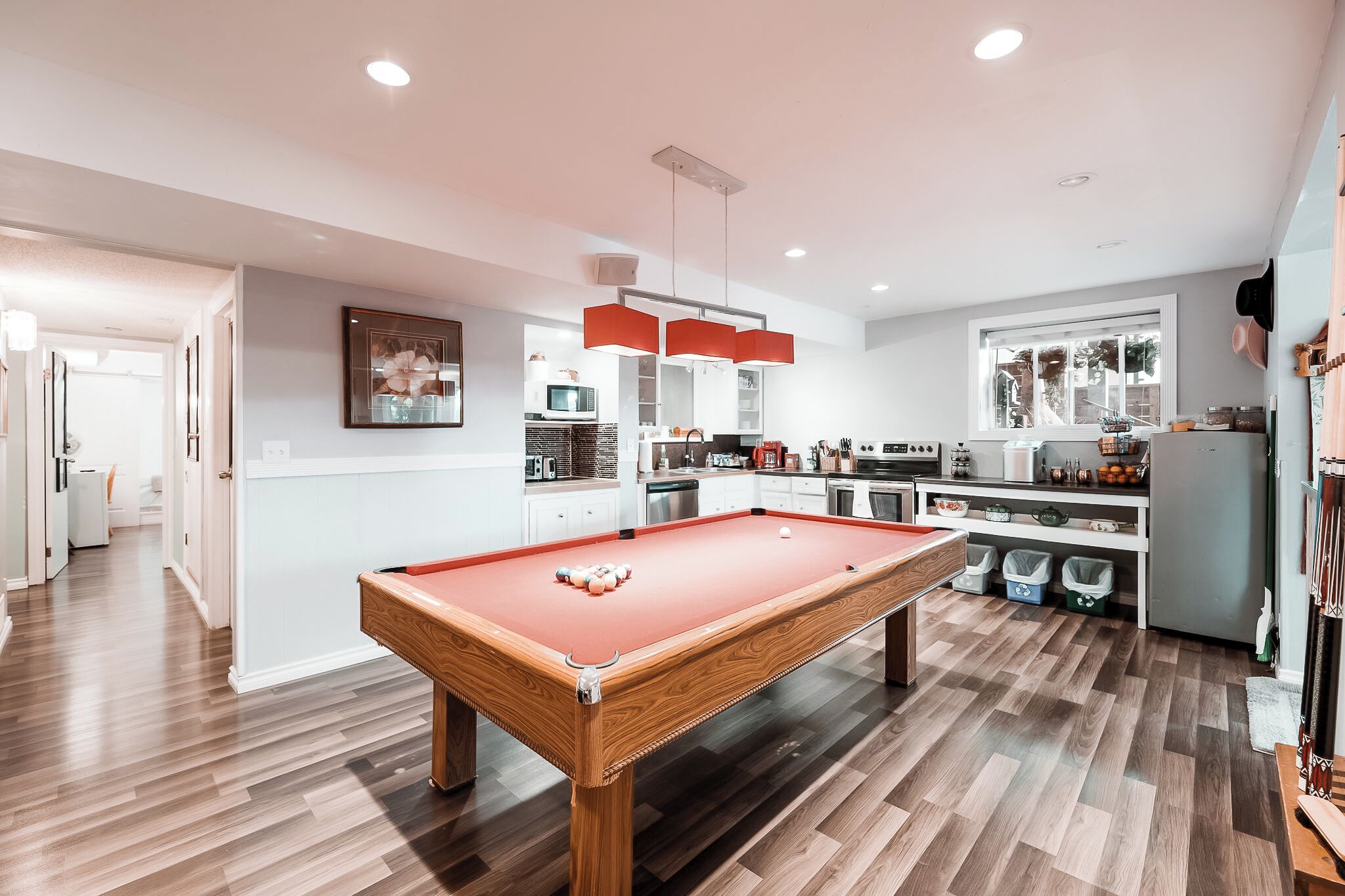 A modern kitchen with a pool table, wooden flooring, and a bright pendant light.