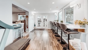 A modern kitchen with a bar area, wooden flooring, and a view through glass doors. - Along River Ridge (Calgary)