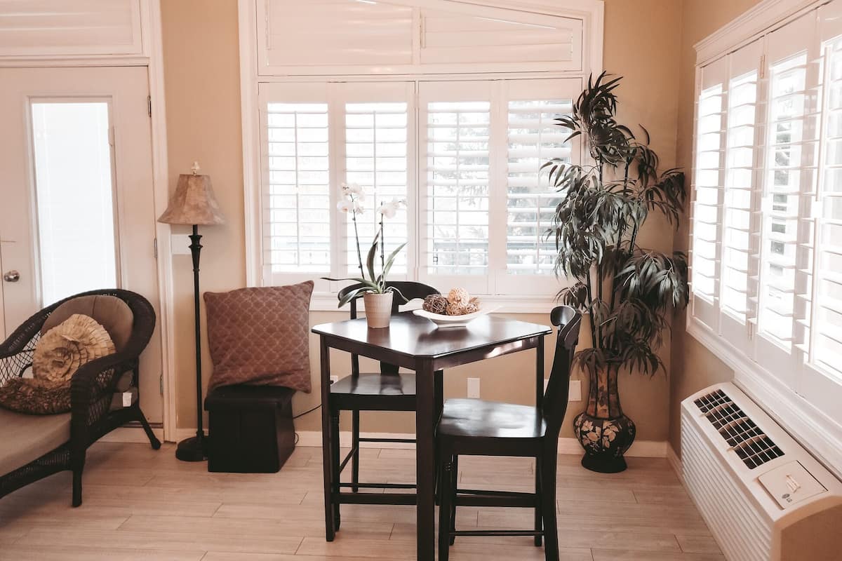 A dining area with a wooden table, chairs, a chandelier, a potted plant, and a radiator.