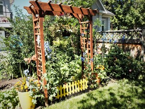 A wooden arbor with climbing plants and flowers, surrounded by a yellow picket fence and a garden bed. - Along River Ridge (Calgary)