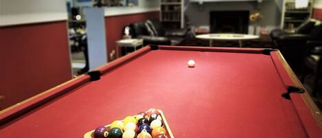 A pool table with a triangular rack of billiard balls in a room with a fireplace and bookshelves.