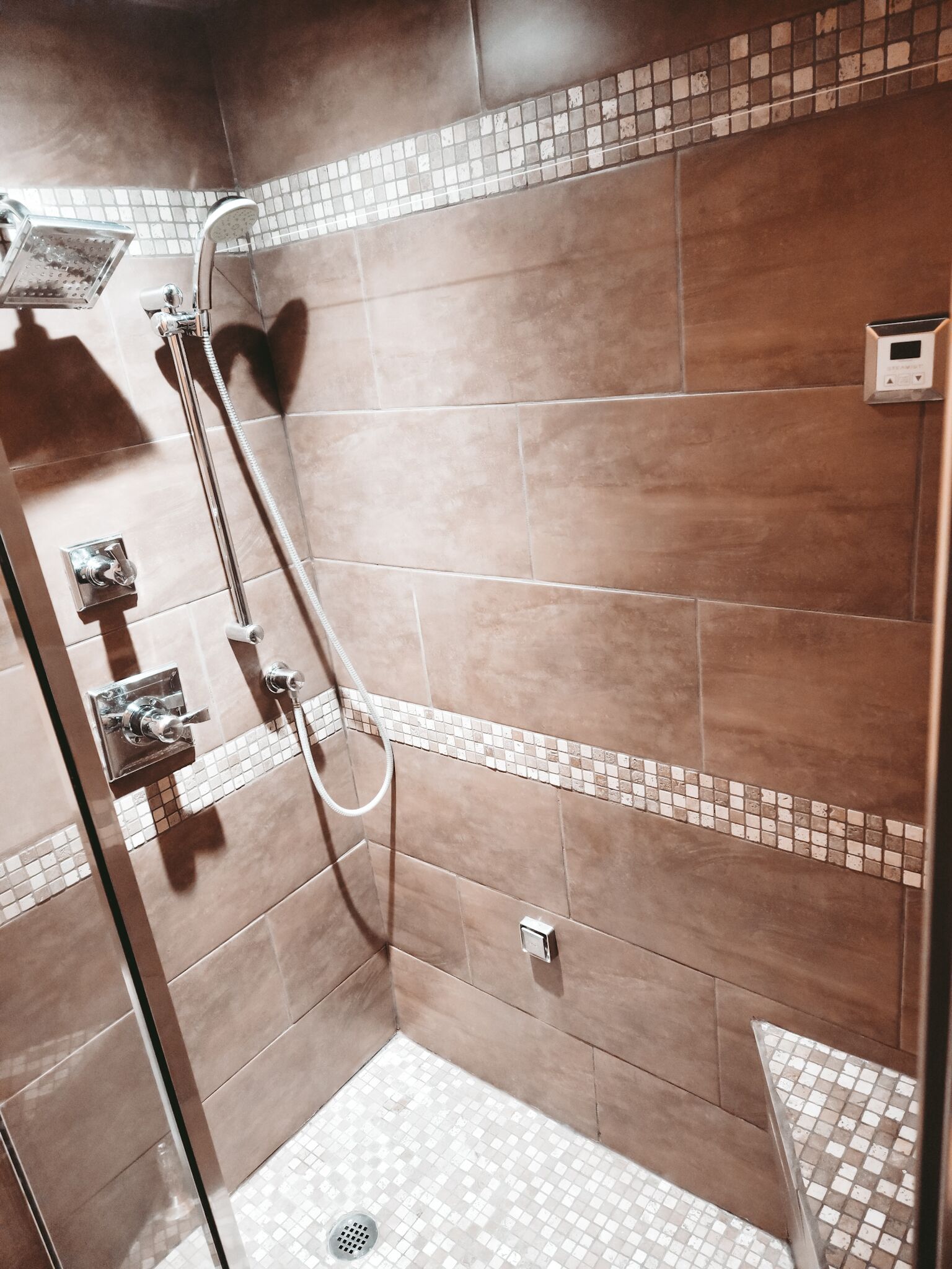 A shower area with a glass door, a handheld showerhead, and a control panel.