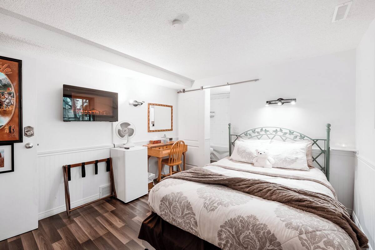 A bedroom with a bed, a desk, a chair, a mirror, and a TV.