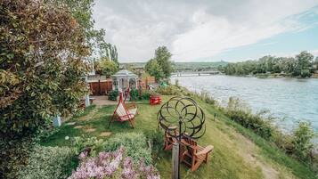 Jardín a la orilla del río con un mirador, sillas mecedoras y una escultura de metal decorativa.