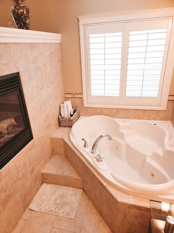 A bathroom with a freestanding bathtub, a window with blinds, a framed picture on the wall, and a small basket with towels. - Along River Ridge (Calgary)