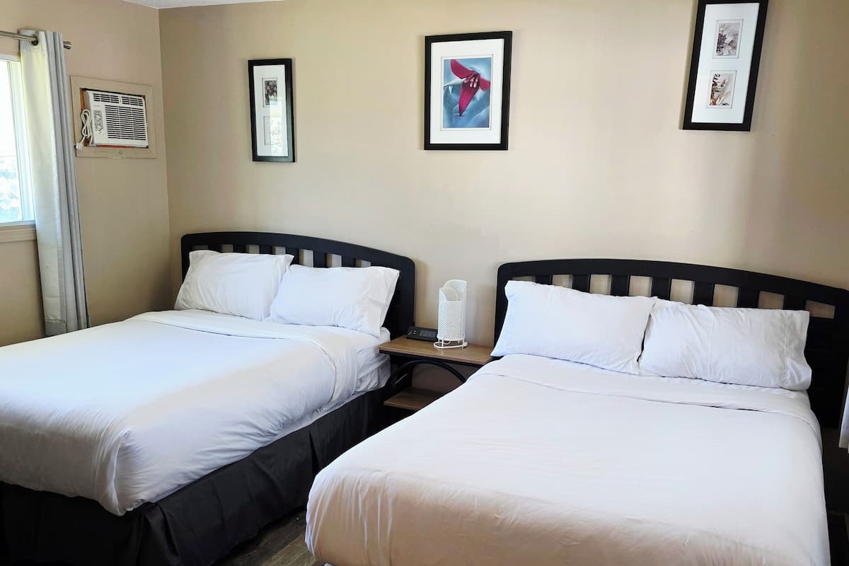 Quarto de hotel com duas camas, mesa de cabeceira com abajur e quadros nas paredes.